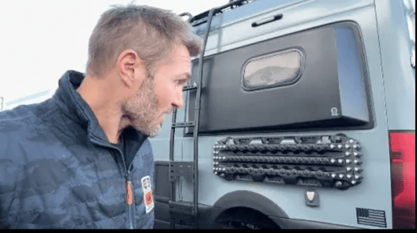 Man examining magnetic mounts holding traction boards on side of Sprinter van for easy access and secure off-road use.
