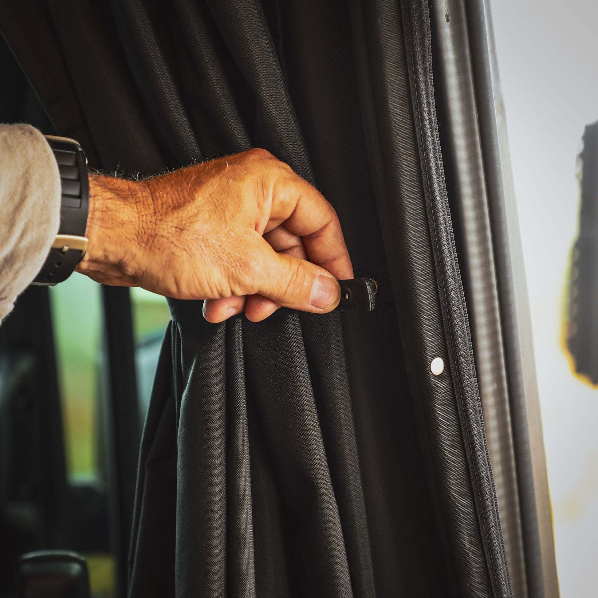 Hand adjusting black CLIMA-SHADE Sprinter Curtain with magnetic tabs for insulation and privacy between cab and living space
