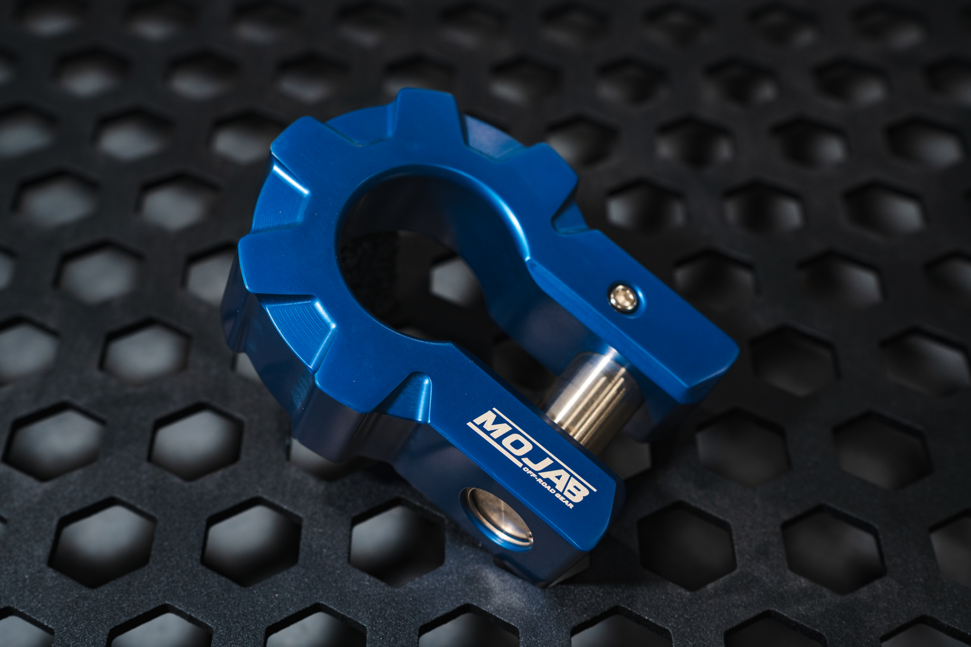 Blue aluminum D-shackle set on textured black surface for off-road recovery.