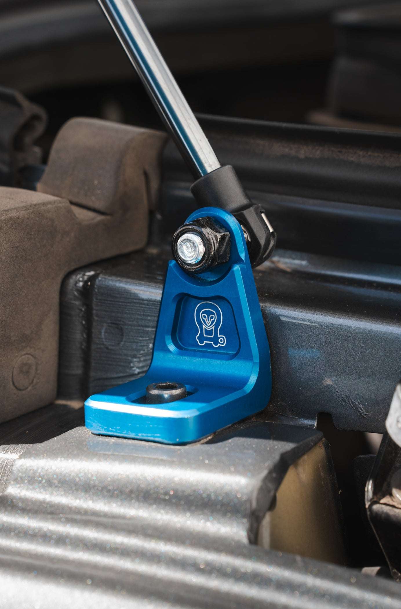 Blue anodized billet aluminum mount of Sprinter Hood Strut Kit installed under hood