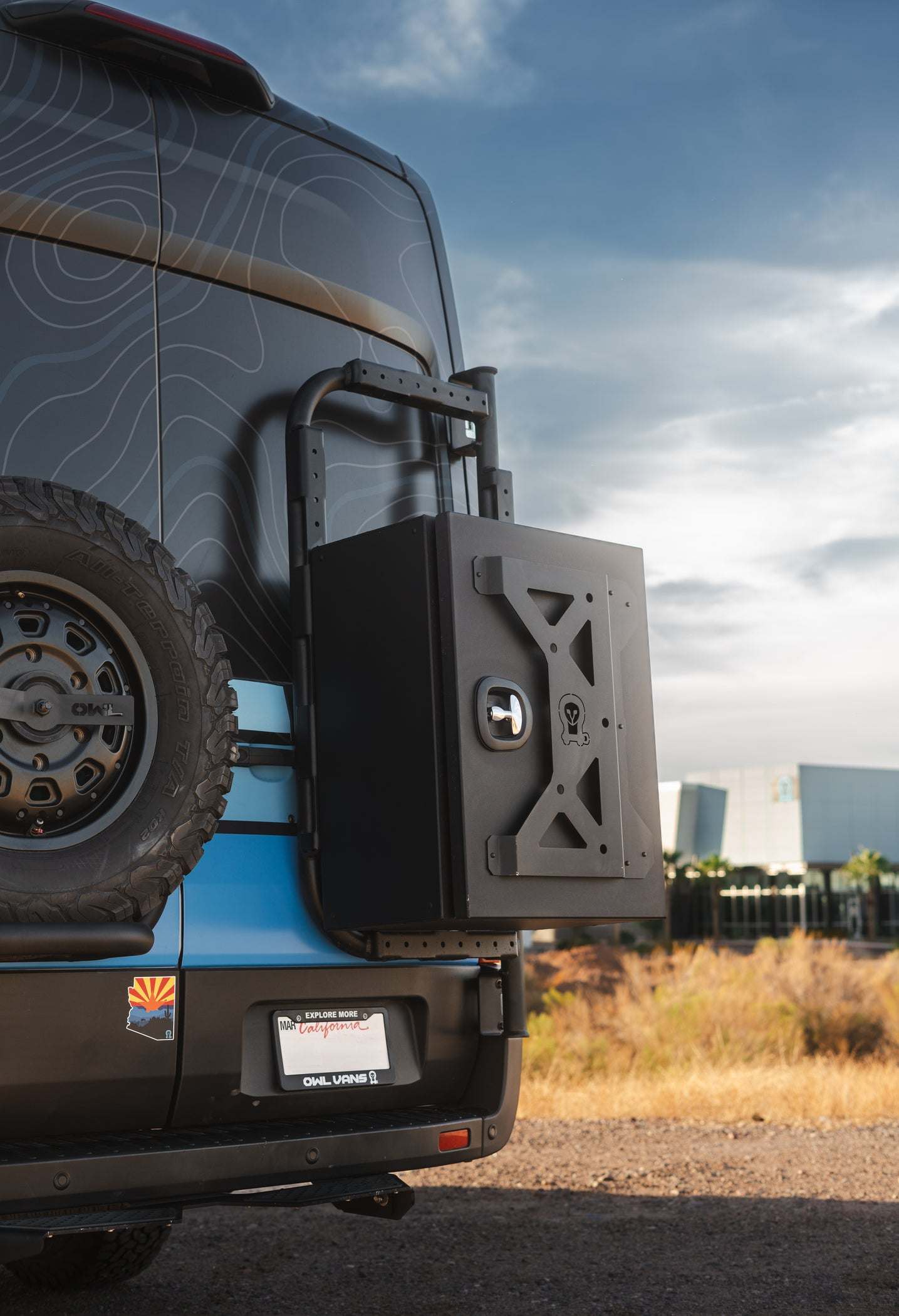 Transit bike rack and box carrier mounted on rear door of van, showing rugged aluminum swing-out frame and modular storage box.