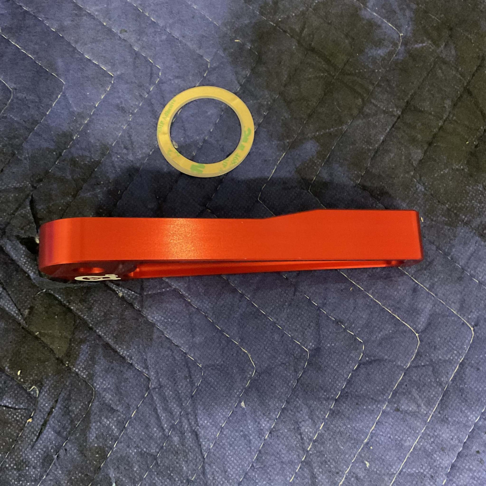 Red Grenadier Hood Release Handle with adhesive gasket on quilted black fabric background