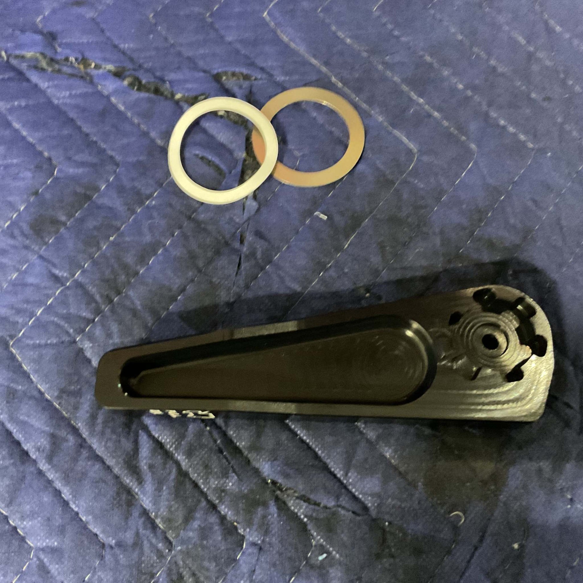 Black Grenadier Hood Release Handle with two metal washers on quilted fabric background