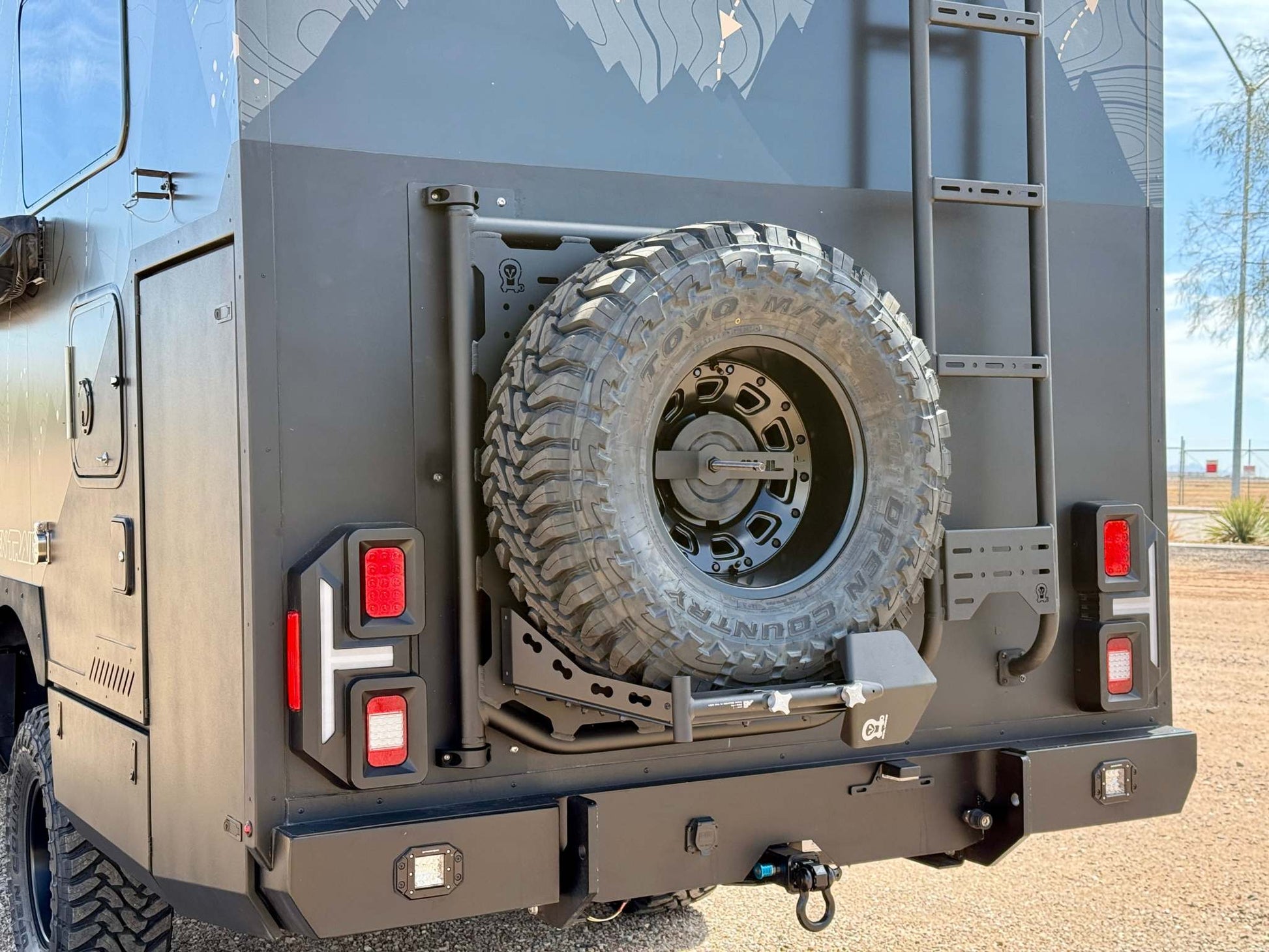 Rear view of OTX Tiffin Open Trail adventure van with spare tire and ladder mounted on matte black exterior