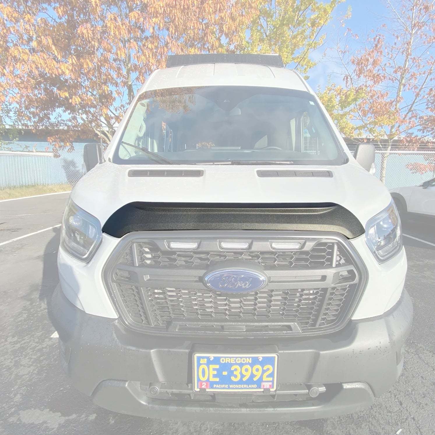 Front view of a white 2021+ Ford Transit van equipped with a black Terrawagen Aero Hood Spoiler under bright daylight