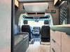 Interior view of OTX Tiffin adventure van showing driver and passenger seats, leather couch, and modern cabinetry.
