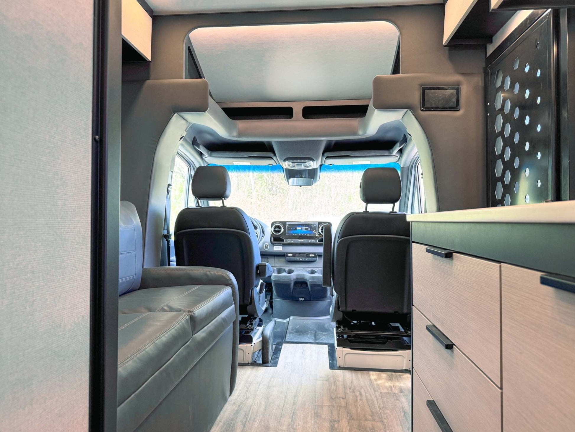Interior view of OTX Tiffin adventure van showing driver and passenger seats, leather couch, and modern cabinetry.