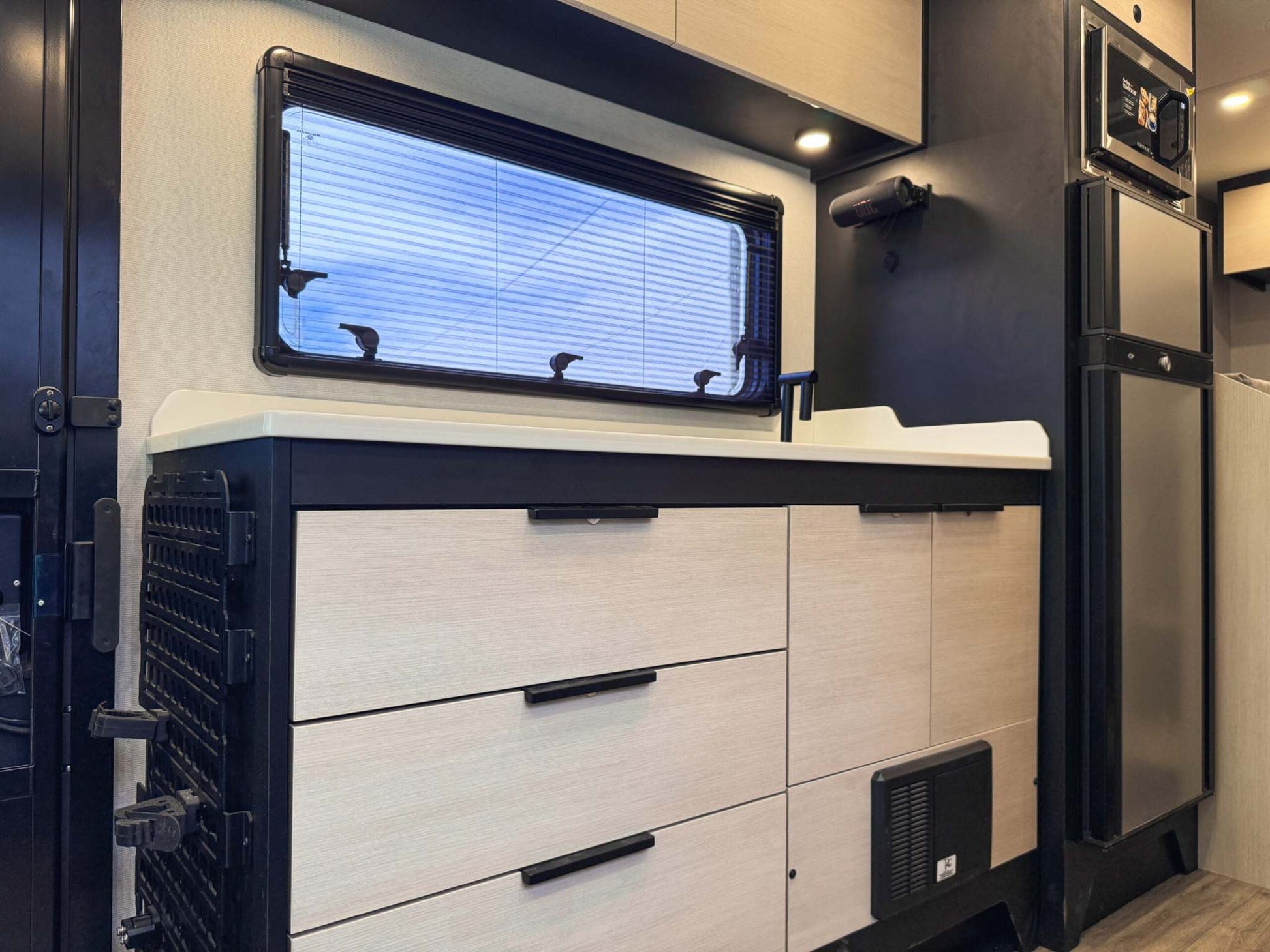 Interior view of OTX Tiffin van kitchen with cabinets, sink, window, and compact refrigerator