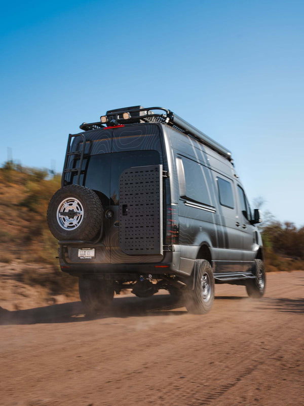 Rear view of black Sprinter van equipped with B2 Sprinter Bike Rack and Box Carrier on dusty road