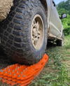 Off-road vehicle using orange steel pin traction boards in muddy terrain.