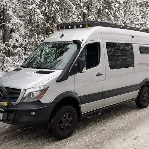 170" Backroad Innovations Sprinter Baja Roof Rack with LED light pods mounted on a white Sprinter van in a snowy forest setting
