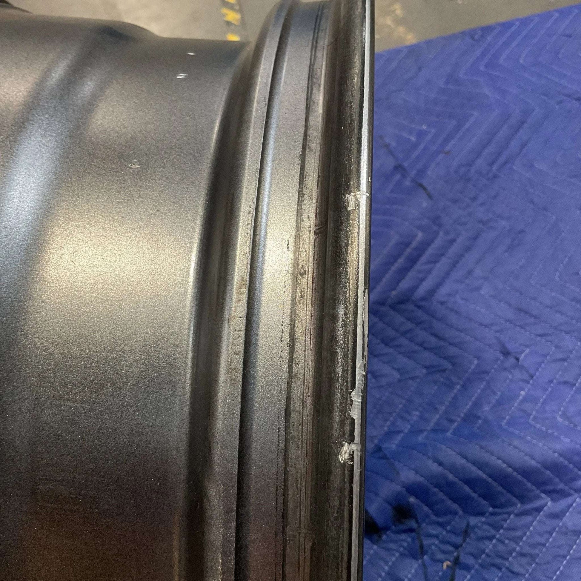 Graphite grey Owl Talon Sprinter wheel with minor scuffs, shown laying on a blue quilted surface.