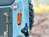 Grenadier Aluminum Rear Door Handle in orange mounted on blue INEOS Grenadier rear door with off-road tire background