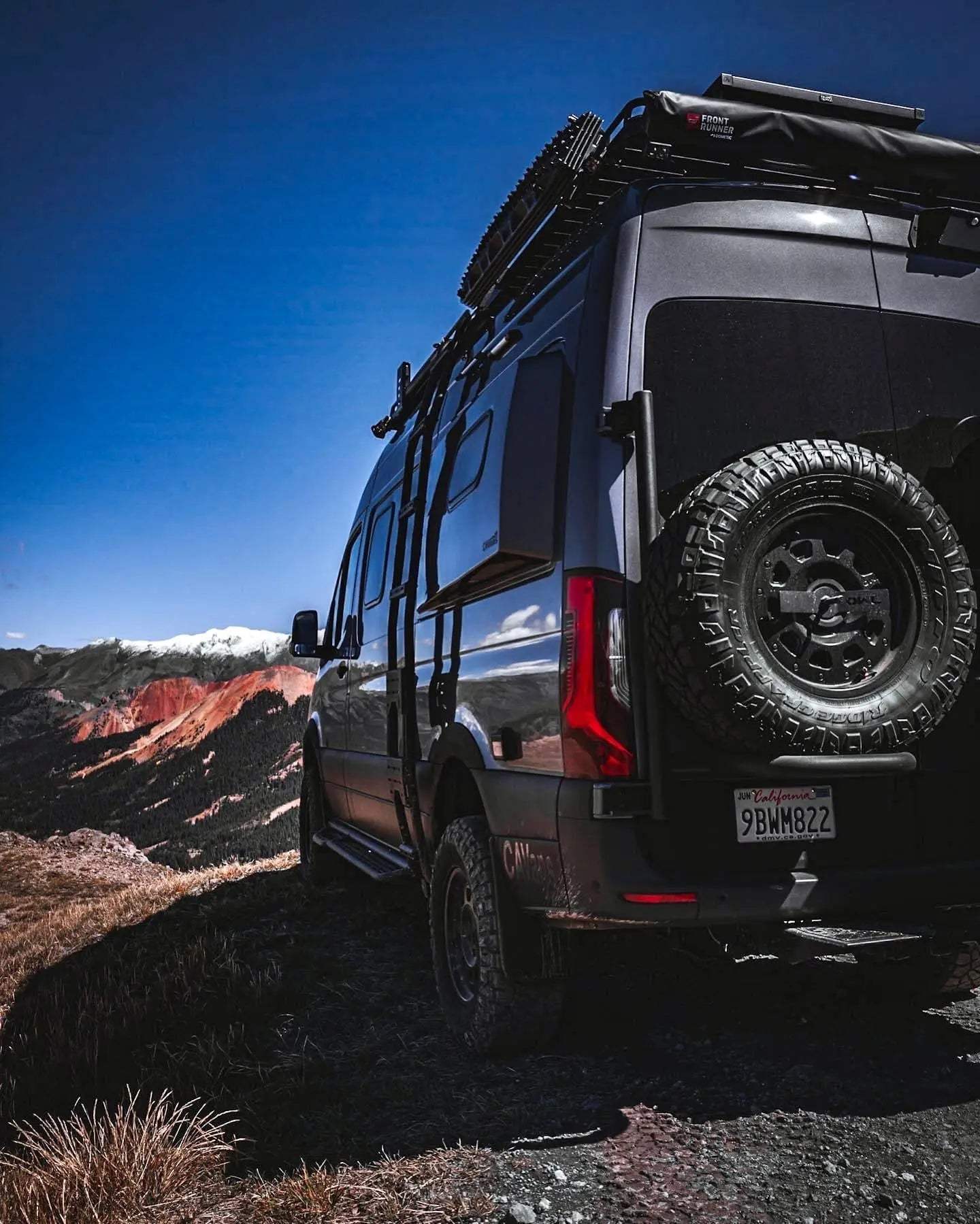 Expedition Tire Carrier mounted on a Sprinter van in rugged terrain.