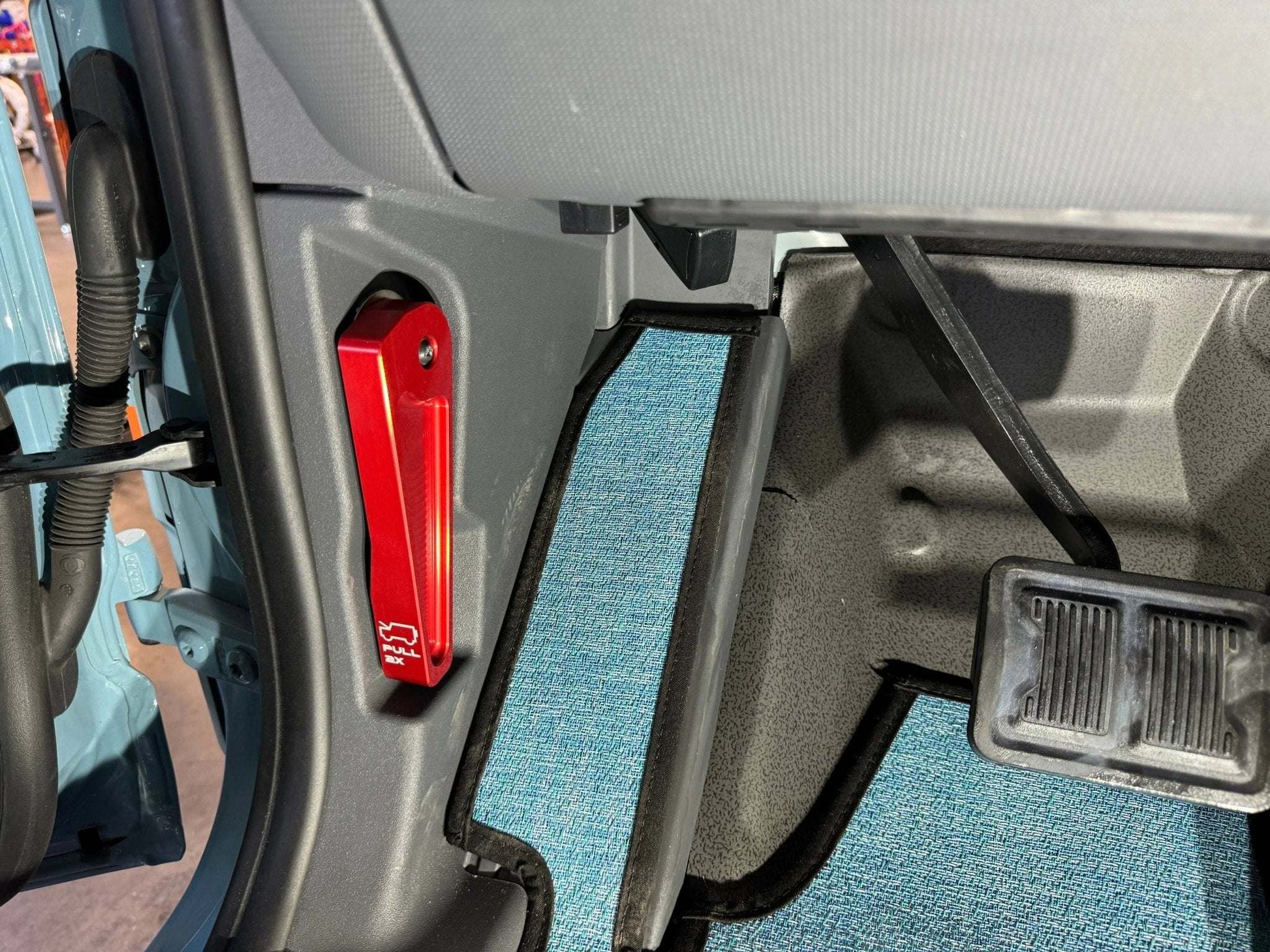 Red Grenadier Hood Release Handle installed on vehicle interior near driver's side pedals