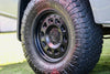 Matte black Super Single Spare Wheel with rugged off-road tire on white vehicle.