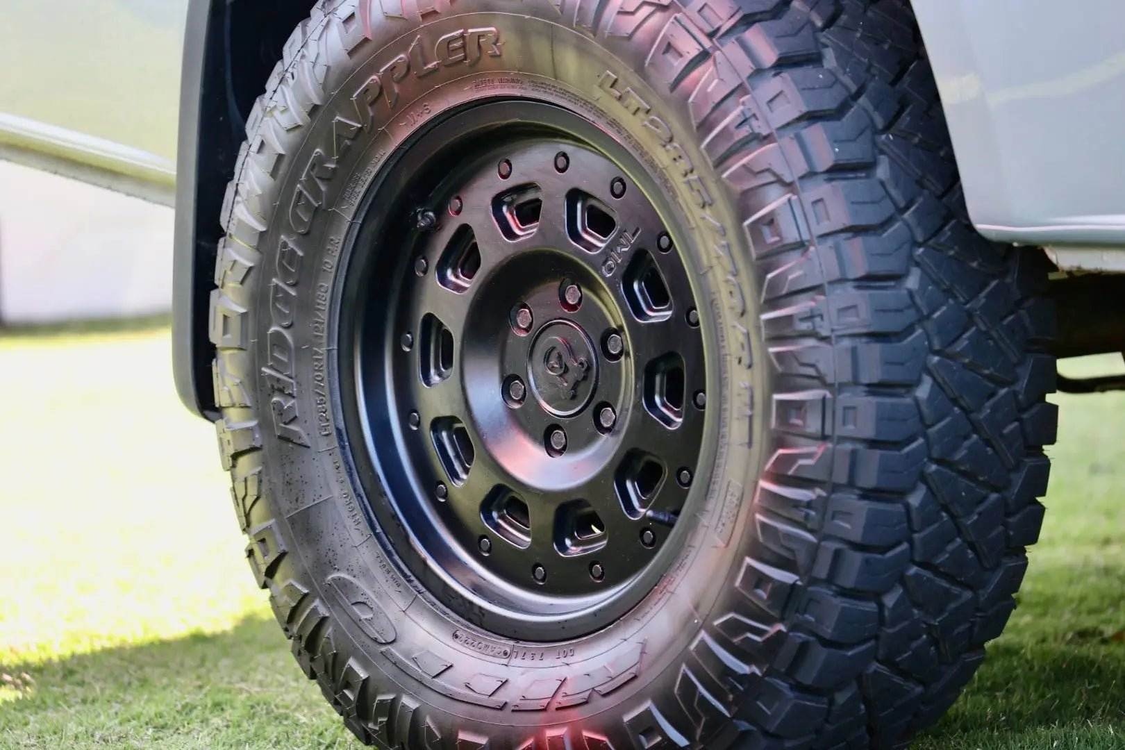 Matte black Super Single Spare Wheel with rugged off-road tire on white vehicle.