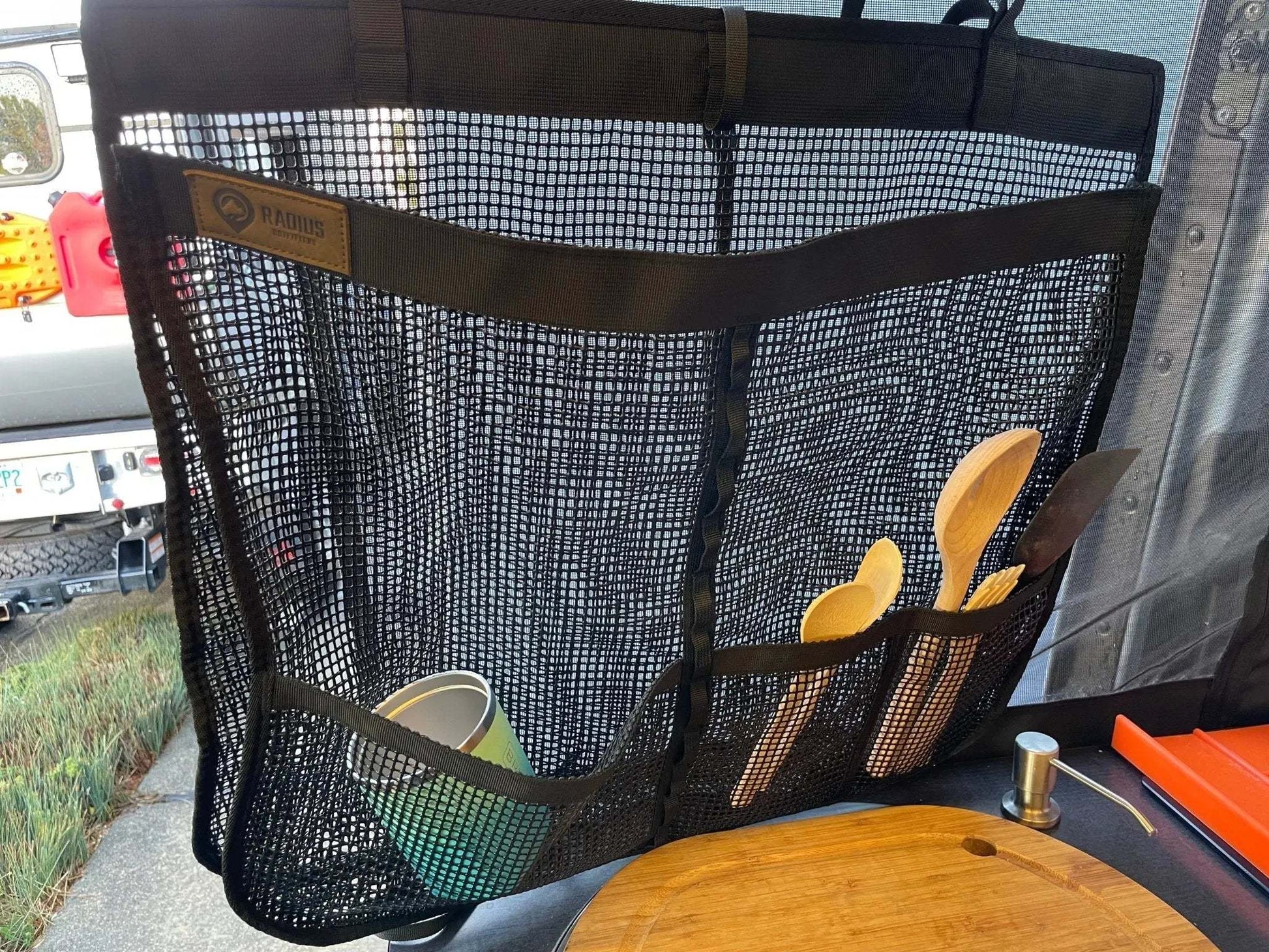 Camp Dish Drying Bag hanging with wooden utensils and cup inside, breathable mesh design for drying and storage.