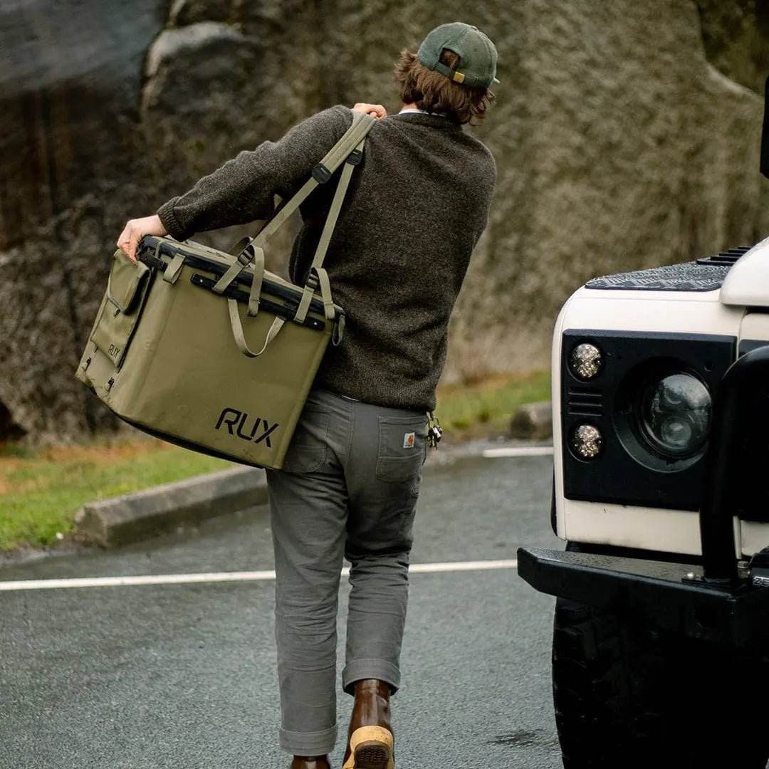 70L Storage Bag being carried by a person near an off-road vehicle, showcasing durability and utility for adventure.