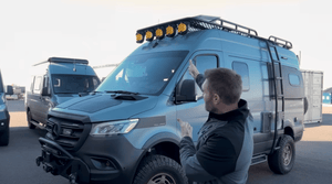 Man pointing at a customized Mercedes Sprinter van equipped for off-road adventure with roof lights and ladder, illustrating tips for Sprinter repairs.