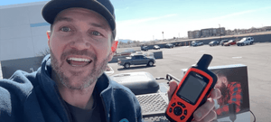 Man outdoors in parking lot holding a Garmin handheld satellite communicator, demonstrating ways to stay connected off-grid.