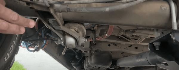 Underside view of a van showing the bottom shock bracket and suspension components with a hand pointing at the bracket.