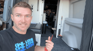 Man demonstrating how to fix rust under the rear trim of a van with tools inside the vehicle.