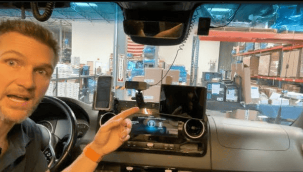 Man demonstrating Ram Ball Mount installed on Sprinter Van dashboard with mounted phone and GPS device in warehouse setting