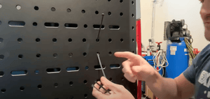 Man demonstrating zip tie trick for threading zip tie through holes on black metal van panel in workshop