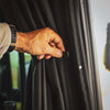 Hand adjusting black CLIMA-SHADE Sprinter Curtain with magnetic tabs for insulation and privacy between cab and living space