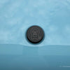 Black billet aluminum INEOS Grenadier hood badge with laser-etched Owl logo on light blue vehicle hood