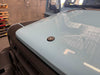 Black billet aluminum owl hood badge installed on light blue INEOS Grenadier vehicle hood in a garage setting