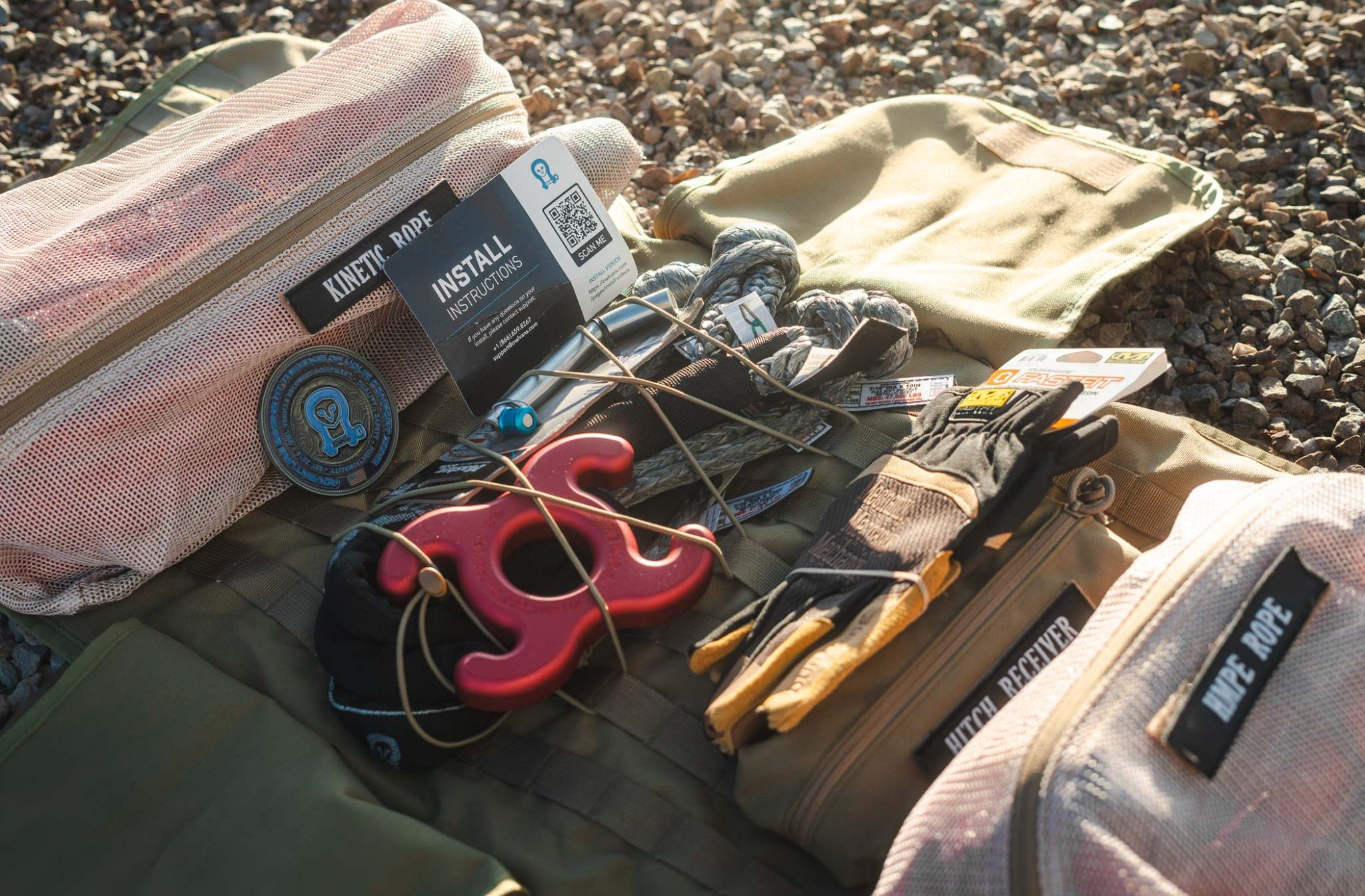 Overland INEOS SUV recovery kit with kinetic rope, gloves, modular MOLLE bag, and hitch receiver on gravel background