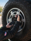 Hands installing Sprinter tire carrier on rear door with rugged tire and metal rim