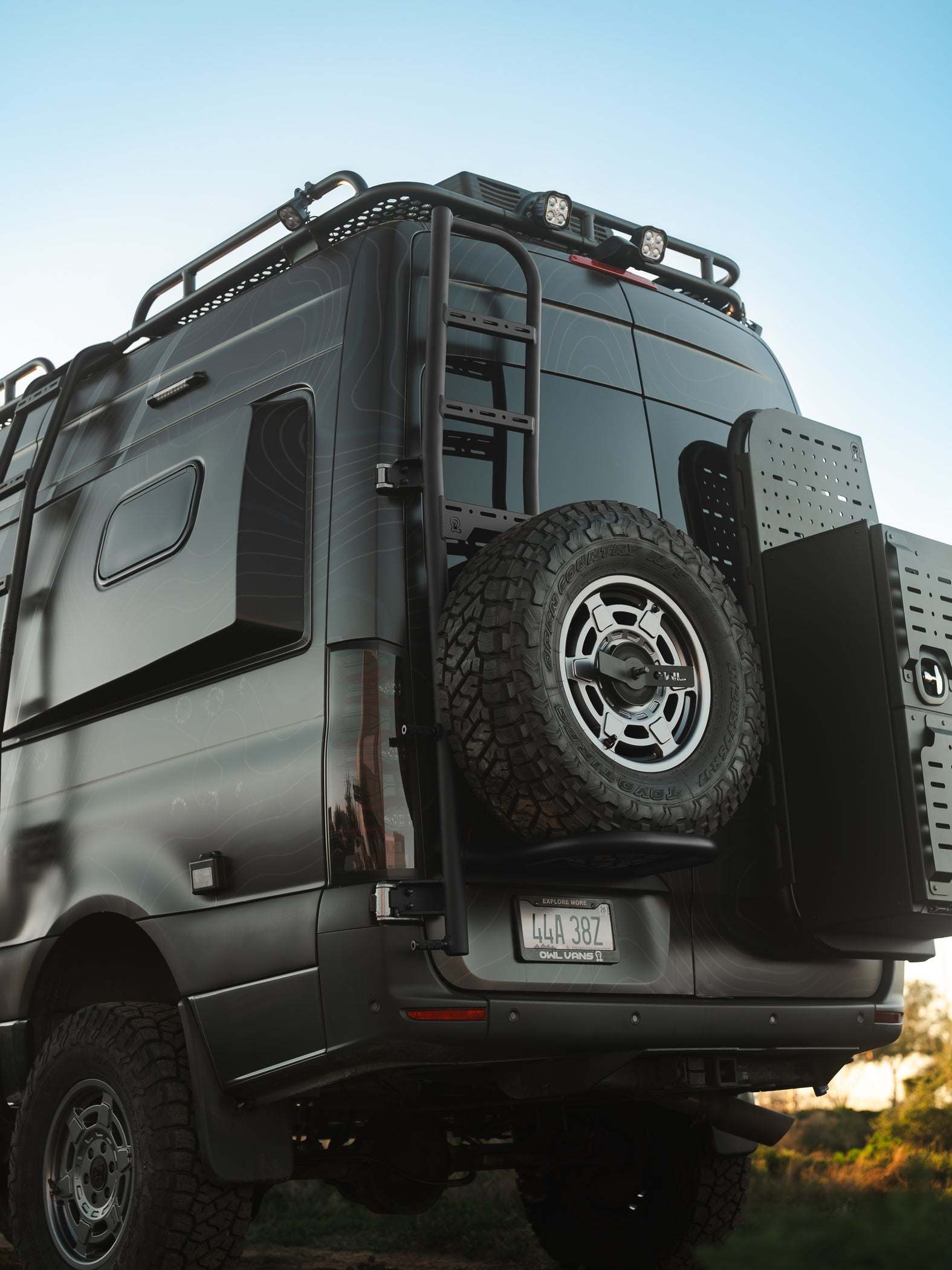 Sprinter tire carrier and ladder mounted on black 2019+ Sprinter rear door with roof rack and gear storage
