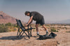 Man setting up Outer Limits Camp Chair on rocky desert terrain with carrying bag nearby