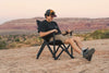 Man sitting comfortably in black Outer Limits Camp Chair on rocky terrain with scenic desert background