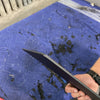 Hand holding a black Grenadier Fender Armor plate on a blue padded surface in a workshop setting