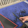 Grenadier fender armor plates with adhesive backing on a blue padded surface and a hand holding one plate edge
