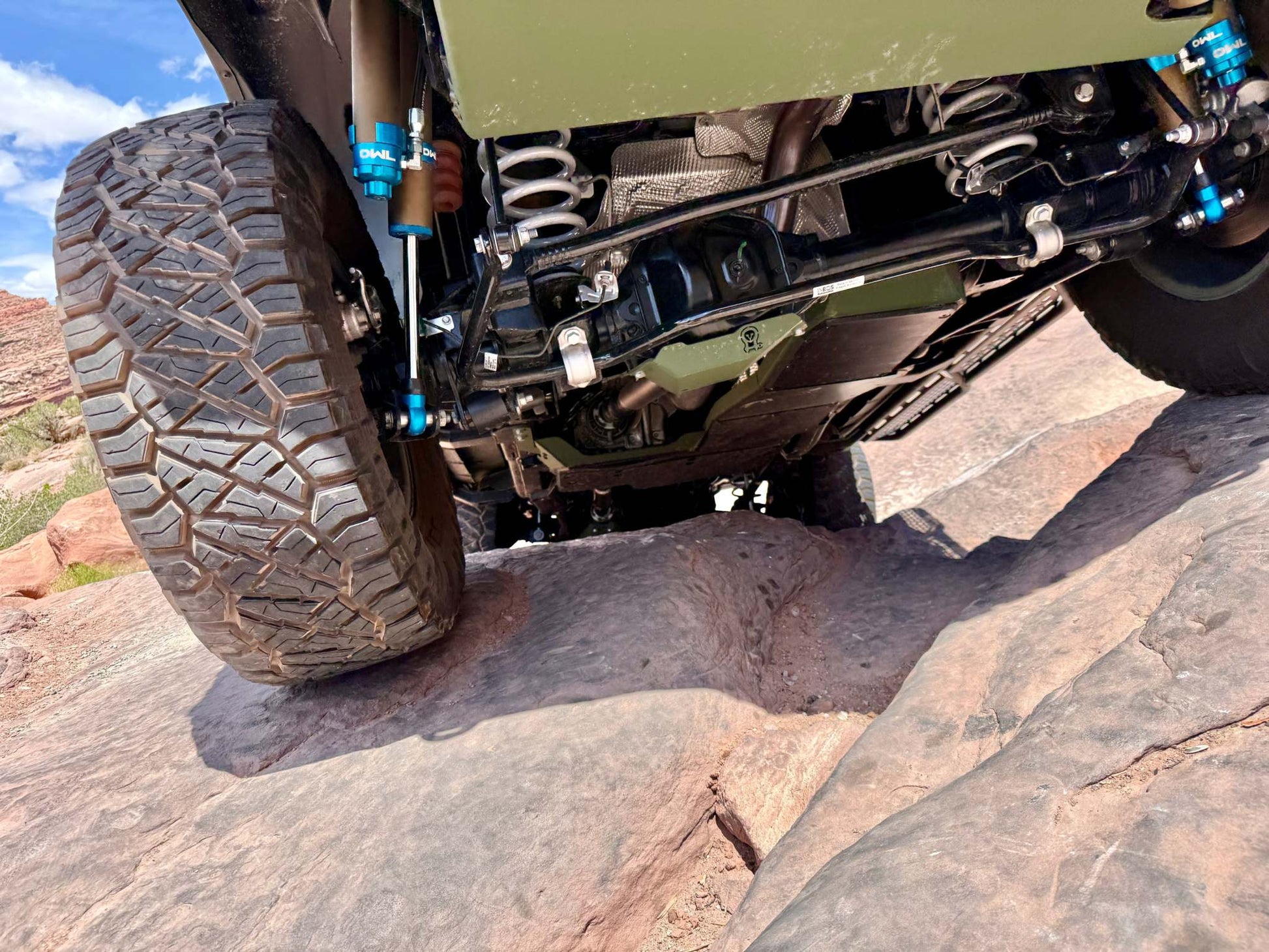 Grenadier Suspension - Underside view of a vehicle equipped with Owl 4" Lift TrailFlo Suspension navigating over rocky terrain