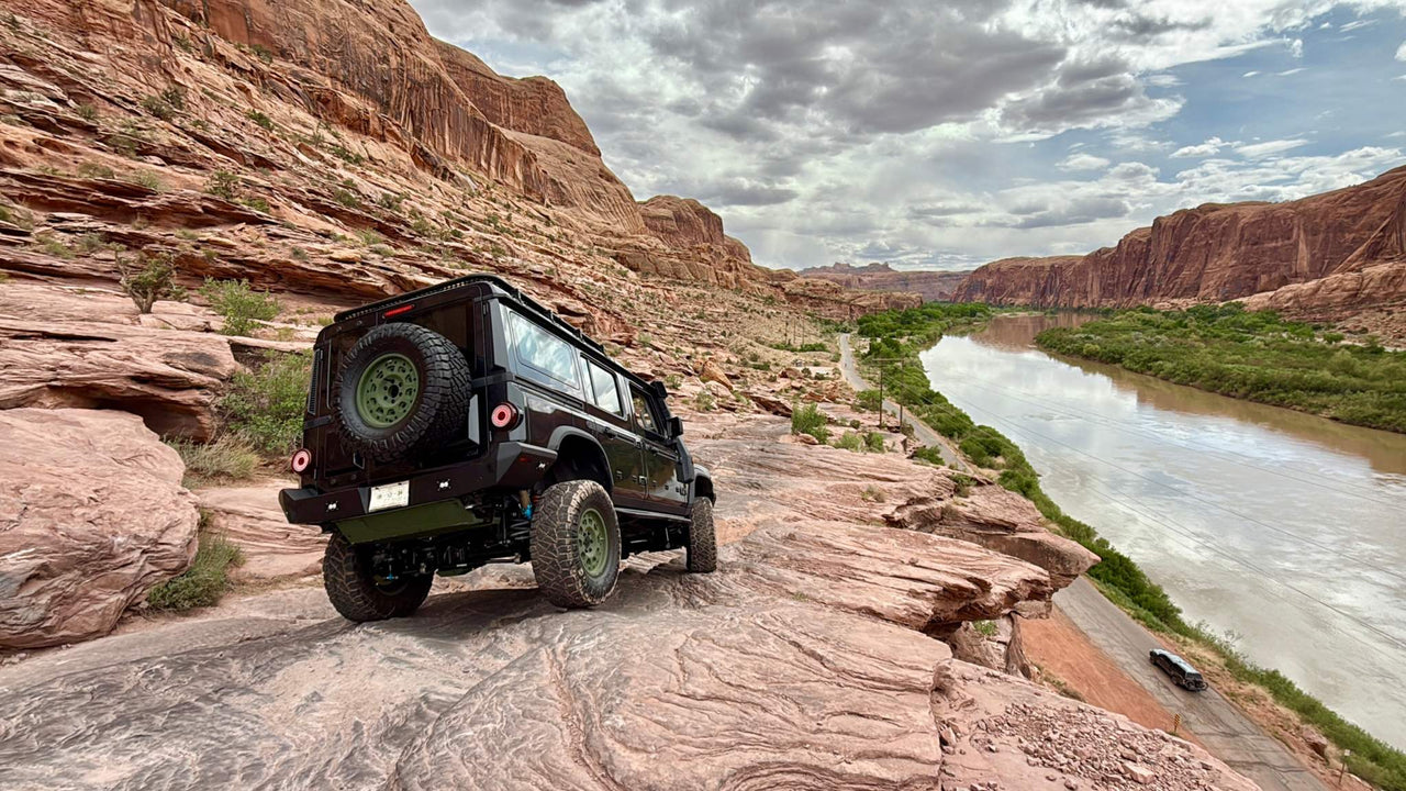INEOS Grenadier off-road vehicle with steel high clearance rear bumper on rocky terrain near river and cliffs