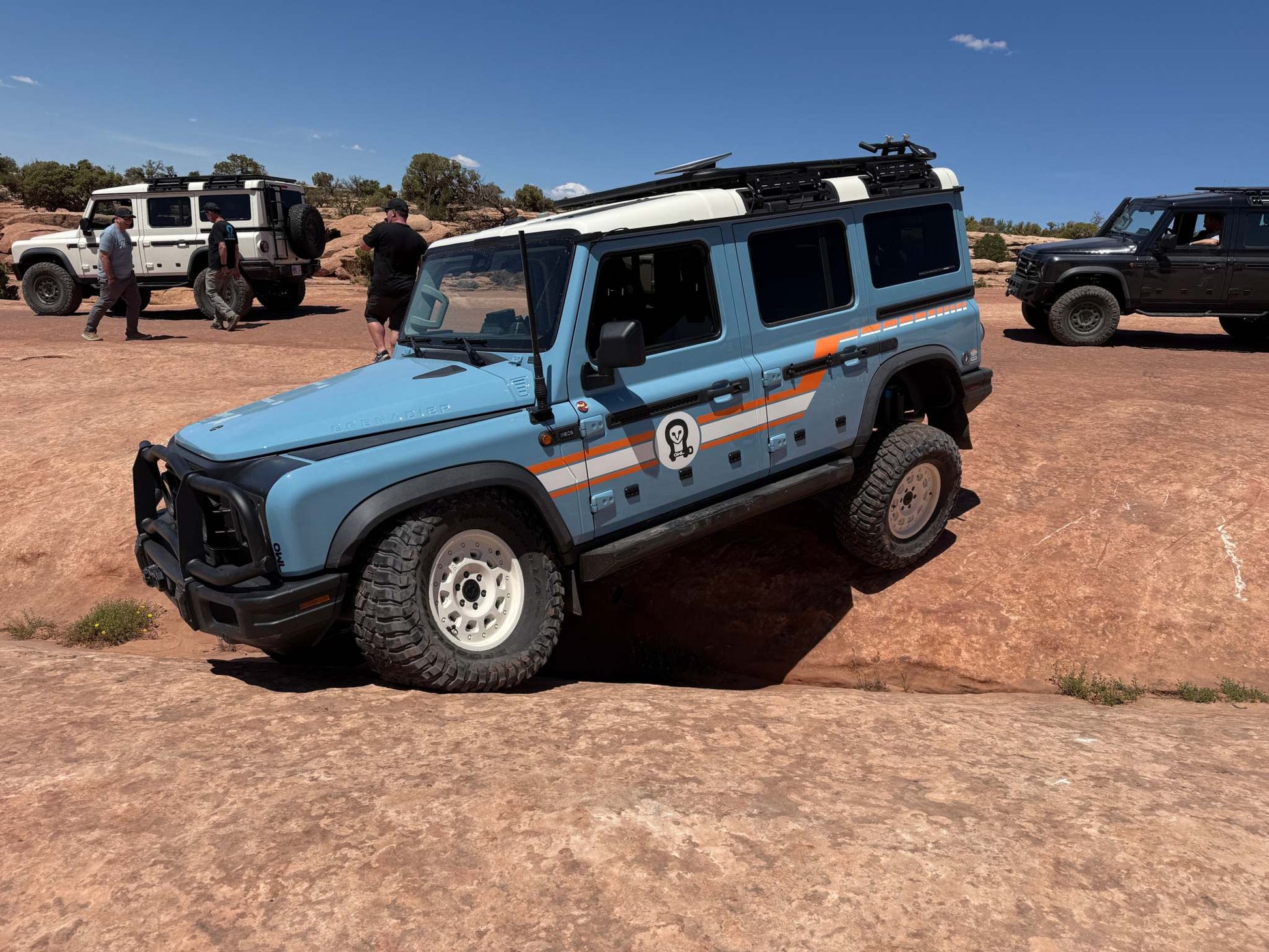 Grenadier Suspension - Blue INEOS Grenadier with Owl 4" Lift TrailFlo Suspension off-roading on rocky terrain with other vehicles in the background