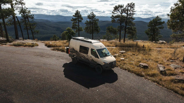 Owl x VanCraft Wasatch Halo Sprinter van driving on mountain road with scenic forest and hills in background