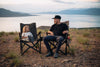 Two people sitting on ergonomic adjustable camp chairs outdoors with mountain and lake view