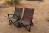 Tan and olive ergonomic camp chairs with armrests set outdoors on gravel ground