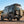 Rear view of a black Sprinter van equipped with a B2 Classic Sprinter Bike Rack and Box Carrier mounted on the rear door, showcasing a spare tire and cargo box in a desert landscape.