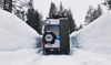 Van with Alpine Box van storage box attached on snowy road between snowbanks in forested area