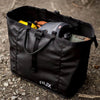 Black versatile RUX 25L Bag packed with camping gear on the ground, easy to carry and organize storage.