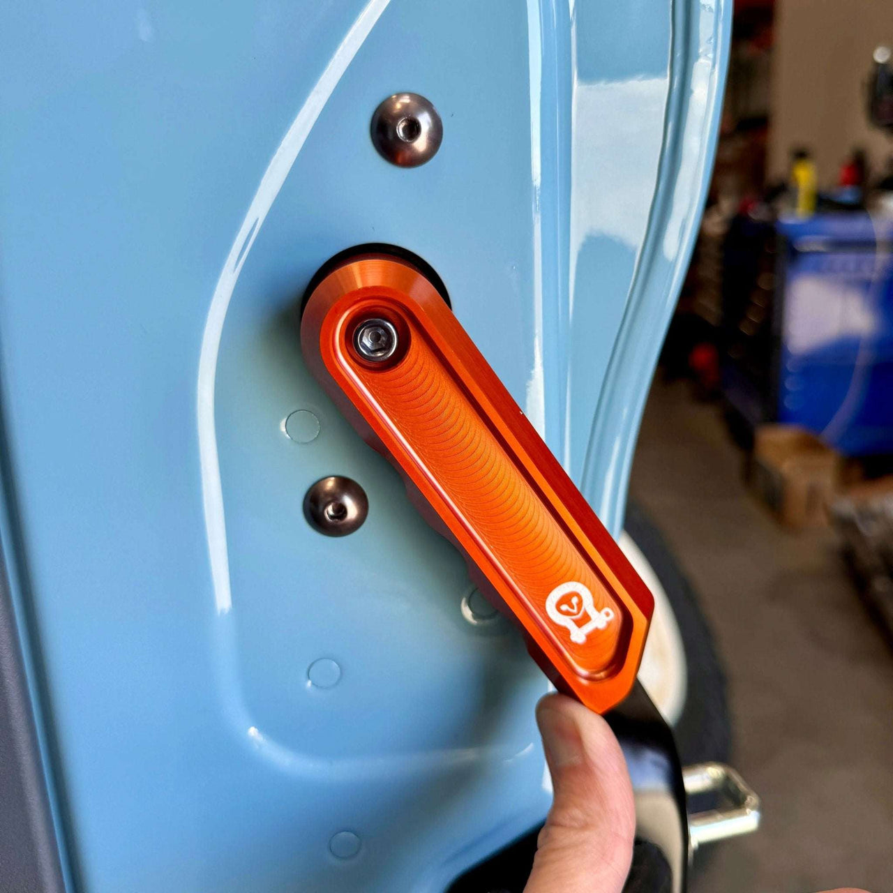 Grenadier Aluminum Rear Door Handle in orange installed on light blue vehicle door, showing durable off-road design