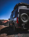 Expedition Tire Carrier mounted on a Sprinter van in rugged terrain.